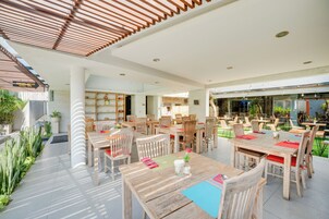 Un espace de restauration en plein air avec des tables et des chaises en bois, entouré de plantes en pot et protégé par une structure en verre.