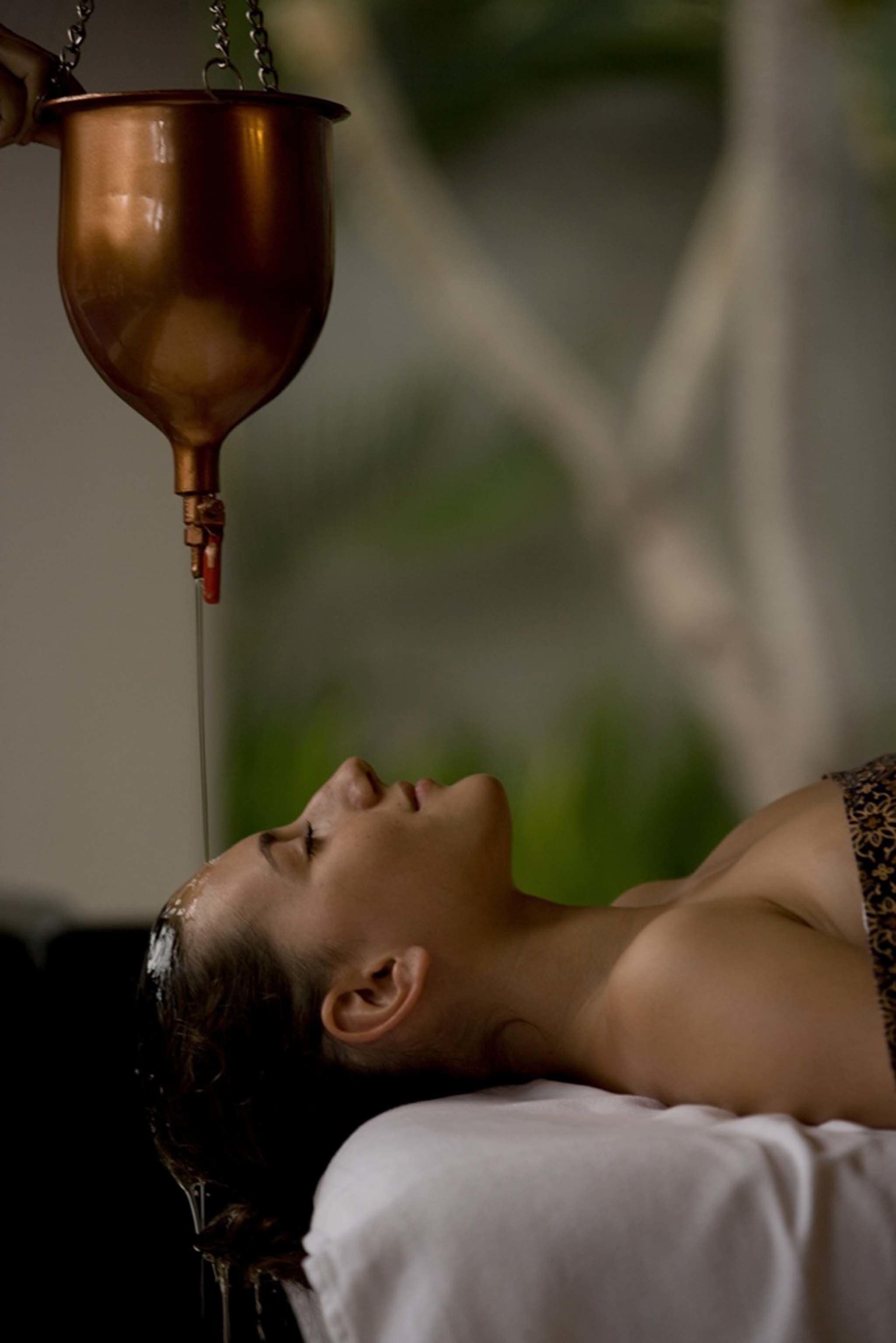A person lying on a bed with water flowing from a copper vessel above.