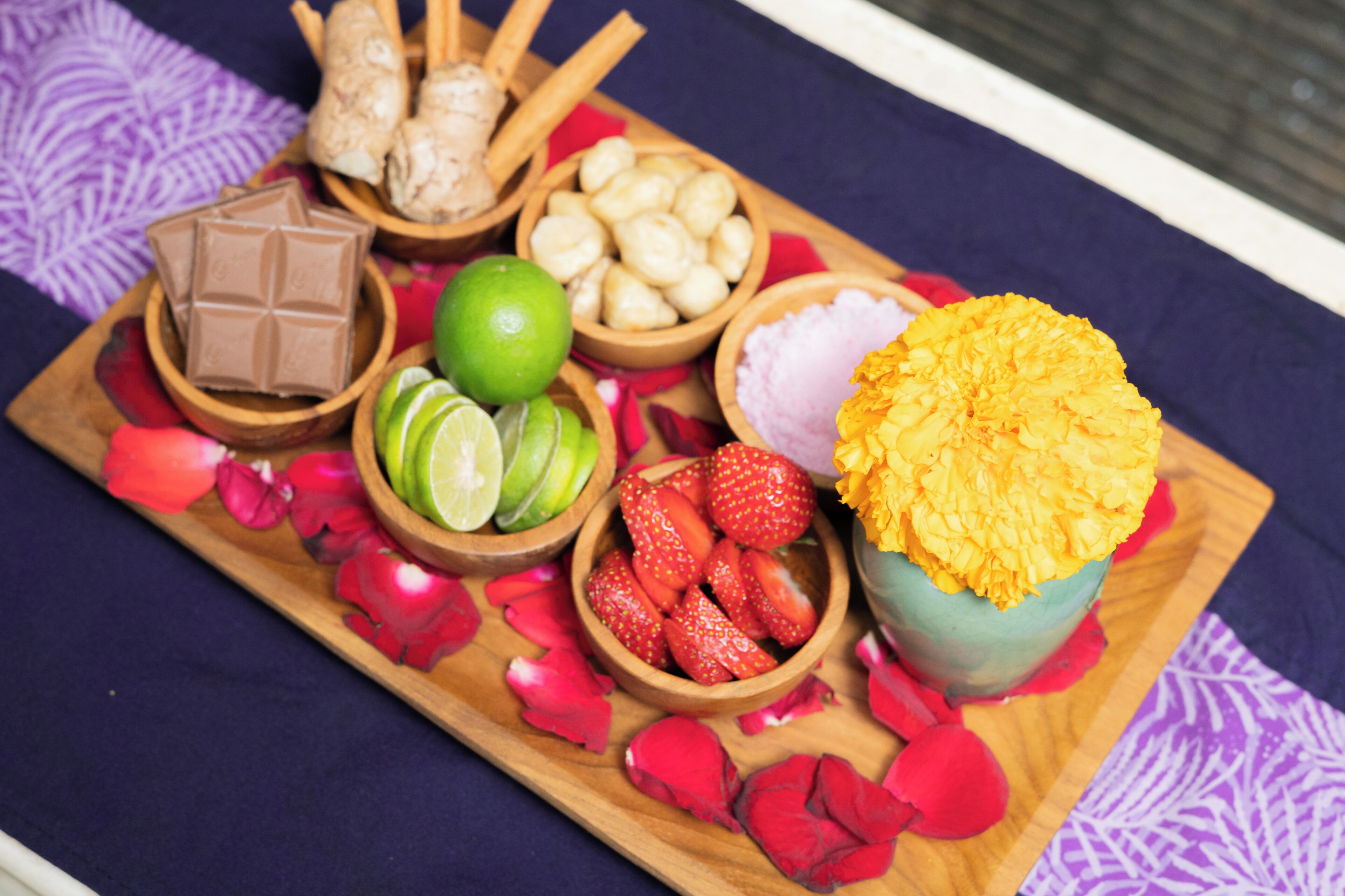 Un plateau en bois contenant divers aliments, notamment du chocolat, des tranches de citron vert, des fraises et un arrangement de fleurs jaunes.