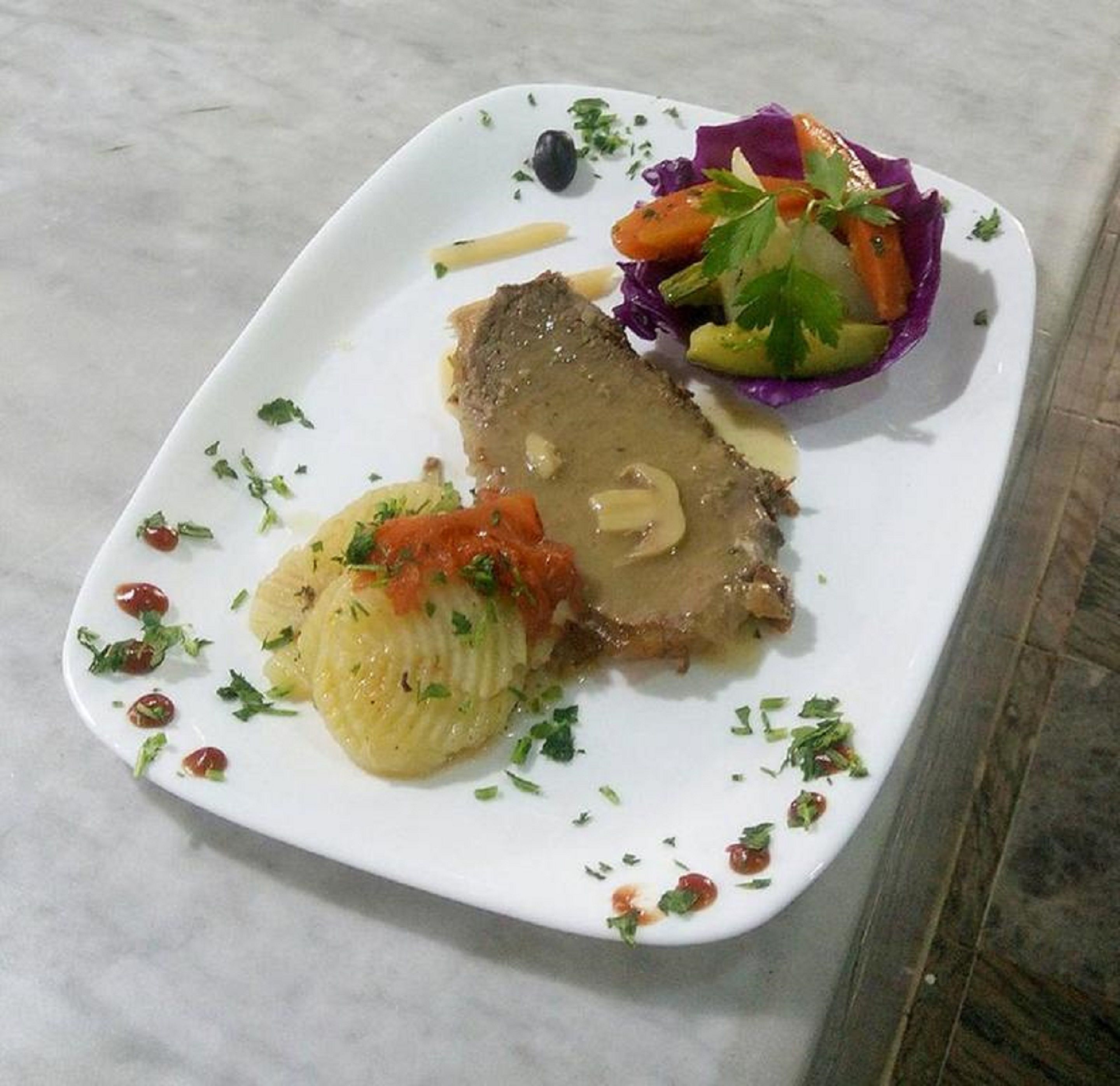 A plate with a meat dish, a side of boiled potatoes, and a mixed vegetable salad.