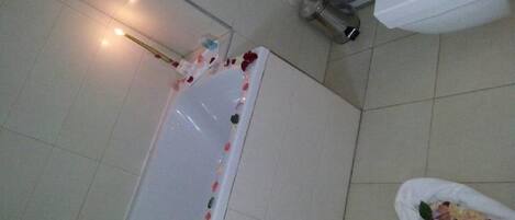 A bathroom with a bathtub, a shower, and a white trash bin.