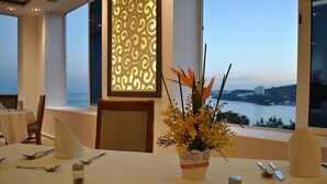 A dining table set with cutlery, a vase with flowers, and a view of the sea.