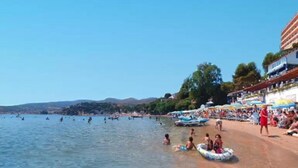 A beach with people swimming and sunbathing, a clear sky, and buildings in the background.