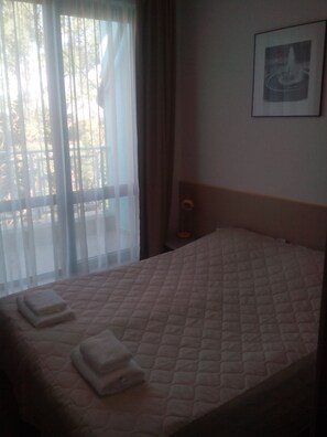 Una habitación de hotel con una cama, una ventana con cortinas translúcidas y un cuadro en la pared.