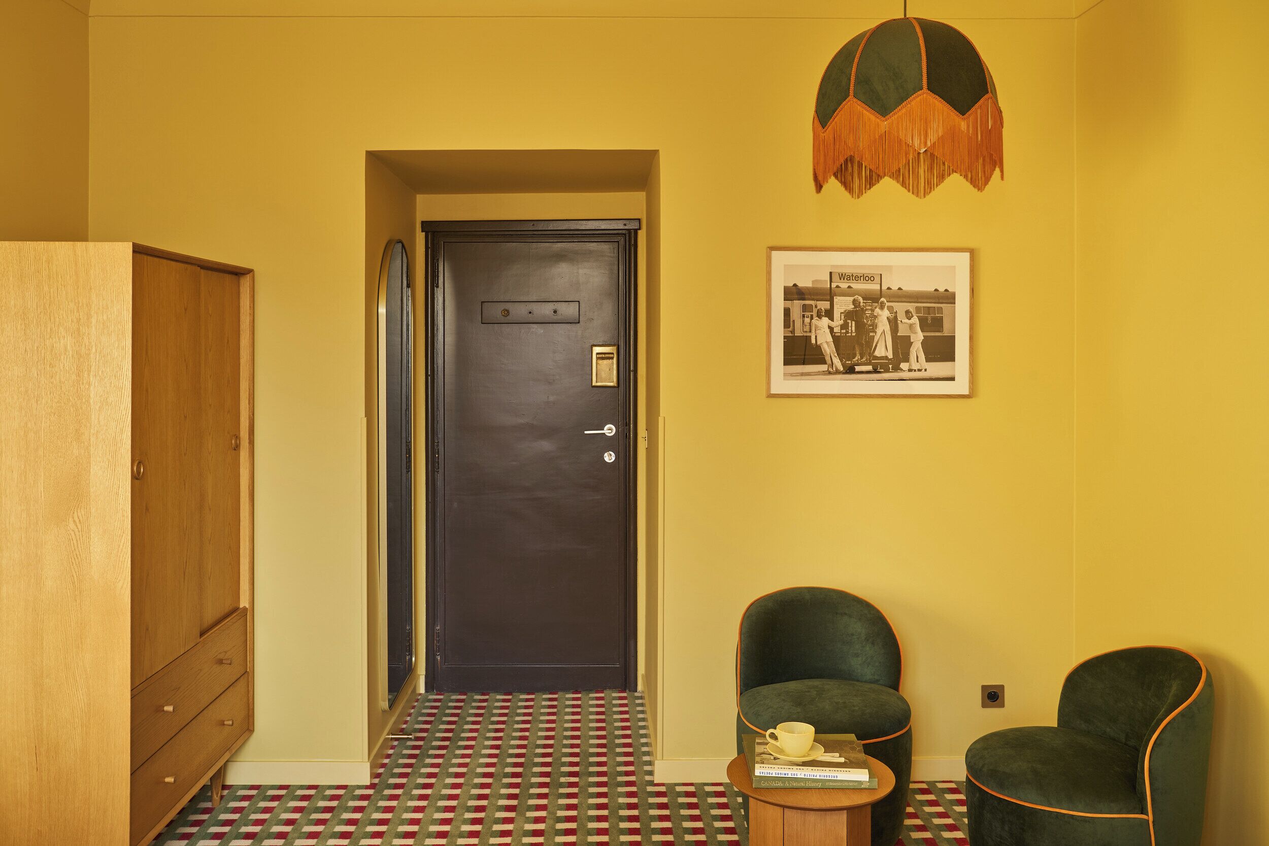 A room with a dark door, a framed photo on the wall, and two green armchairs.