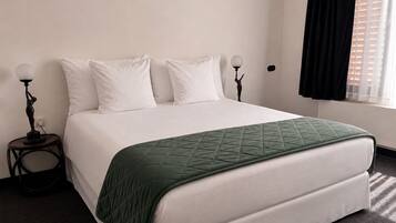 En pænt redt seng med et grønt quilt, hvide puder og et natbord med en lampe.