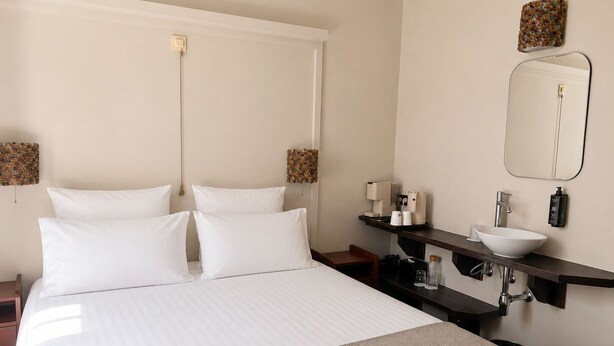 Hotelkamer met een bed, nachtkastje, wastafel, spiegel en een handdoekhouder.