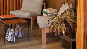 A room with a wooden floor, a chair, a table with magazines, a lamp, and a plant. - Le Berger Latroupe Hotel (Brussels)