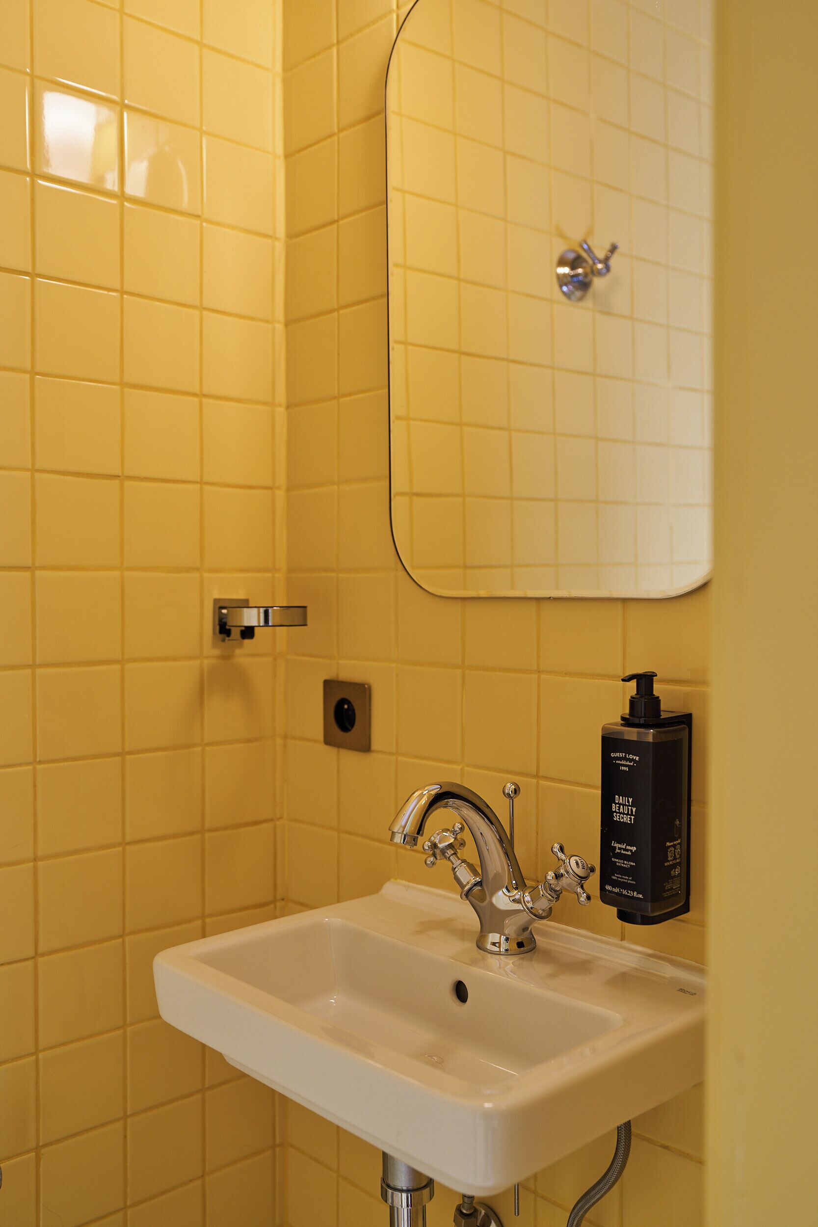 A bathroom with a white sink, a mirror, and a soap dispenser.