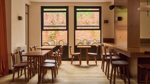 A dining area with wooden tables and chairs, large windows with a brick wall view, and a modern light fixture. - Le Berger Latroupe Hotel (Brussels)