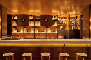 Zona de bar con estanterías de madera, taburetes y una vitrina con copas.