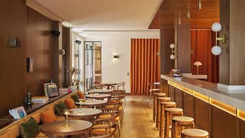 En moderne bar med træmøbler, en disk og et siddeområde med runde borde og stole.
