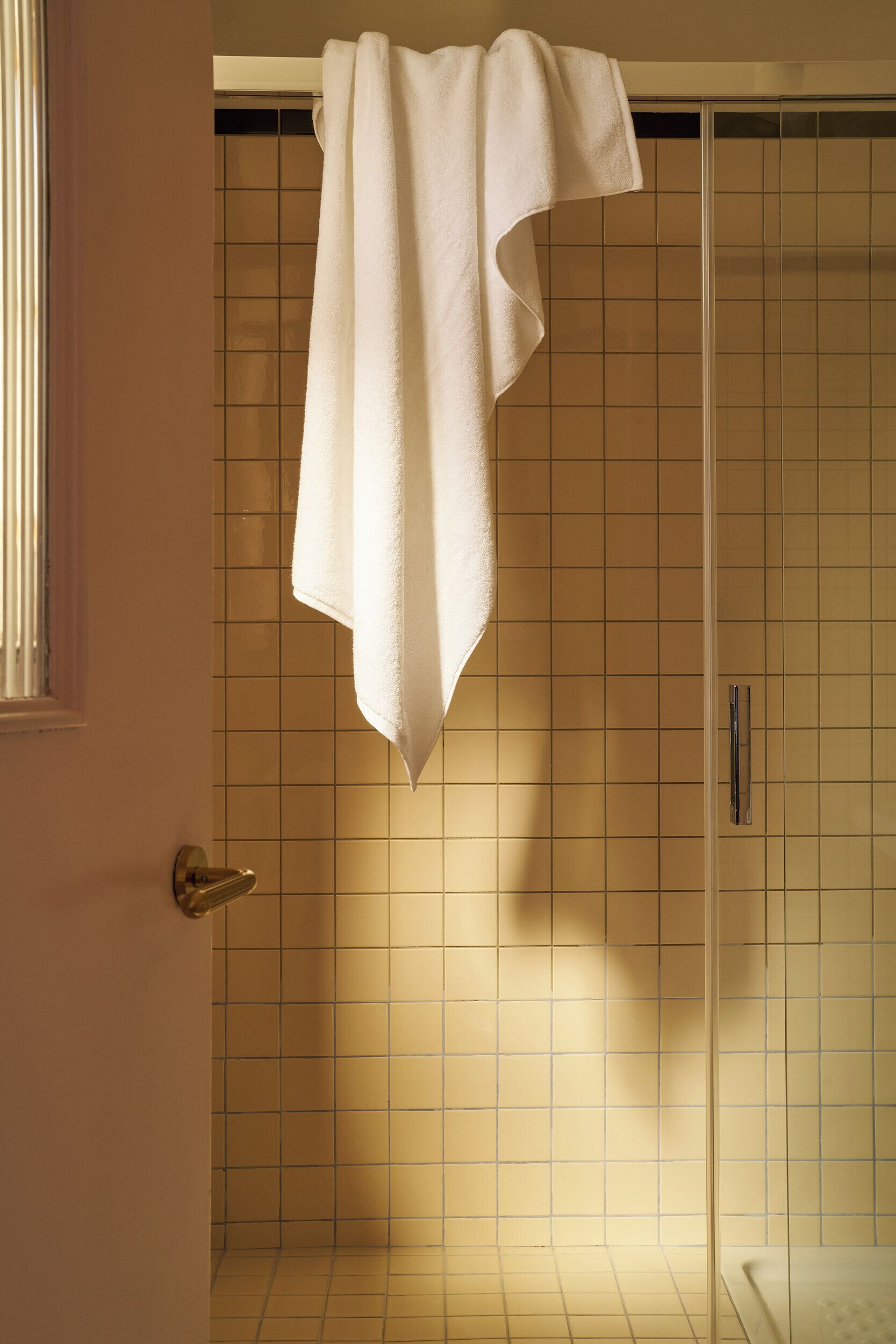 A bathroom with a tiled wall, a shower door, and a towel hanging on the door.
