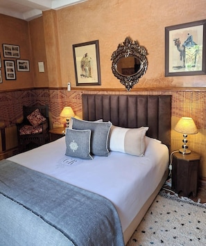 Una habitació d'hotel amb un llit gran, dues làmpades de nit, un mirall decoratiu i quadres a la paret.