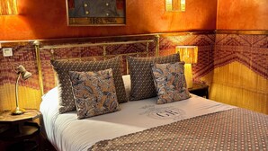A bedroom with a bed, patterned pillows, a headboard, a nightstand, a lamp, and a framed picture on the wall. - Riad El Arsat (Marrakech)