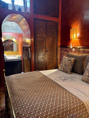Une chambre à coucher avec une couvre-lit à motifs, une grande armoire en bois et un miroir décoratif.