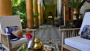 Un interior tradicional con un sofá, una silla, una bandeja con galletas y una tetera, y un jarrón con flores.