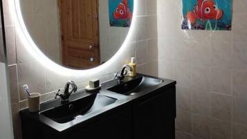 Une salle de bain avec un grand miroir, deux lavabos et une porte en bois.