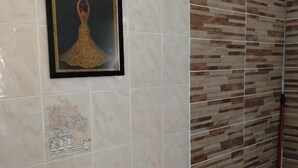 A bathroom with a tiled wall, a framed picture, and a wooden shelf. - Chez Brigitte Guesthouse (Nice)