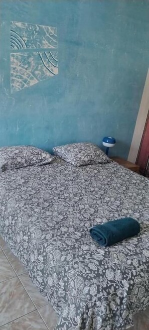 A bedroom with a floral-patterned bedspread, a blue wall, and a small bedside table. - Chez Brigitte Guesthouse (Nice)