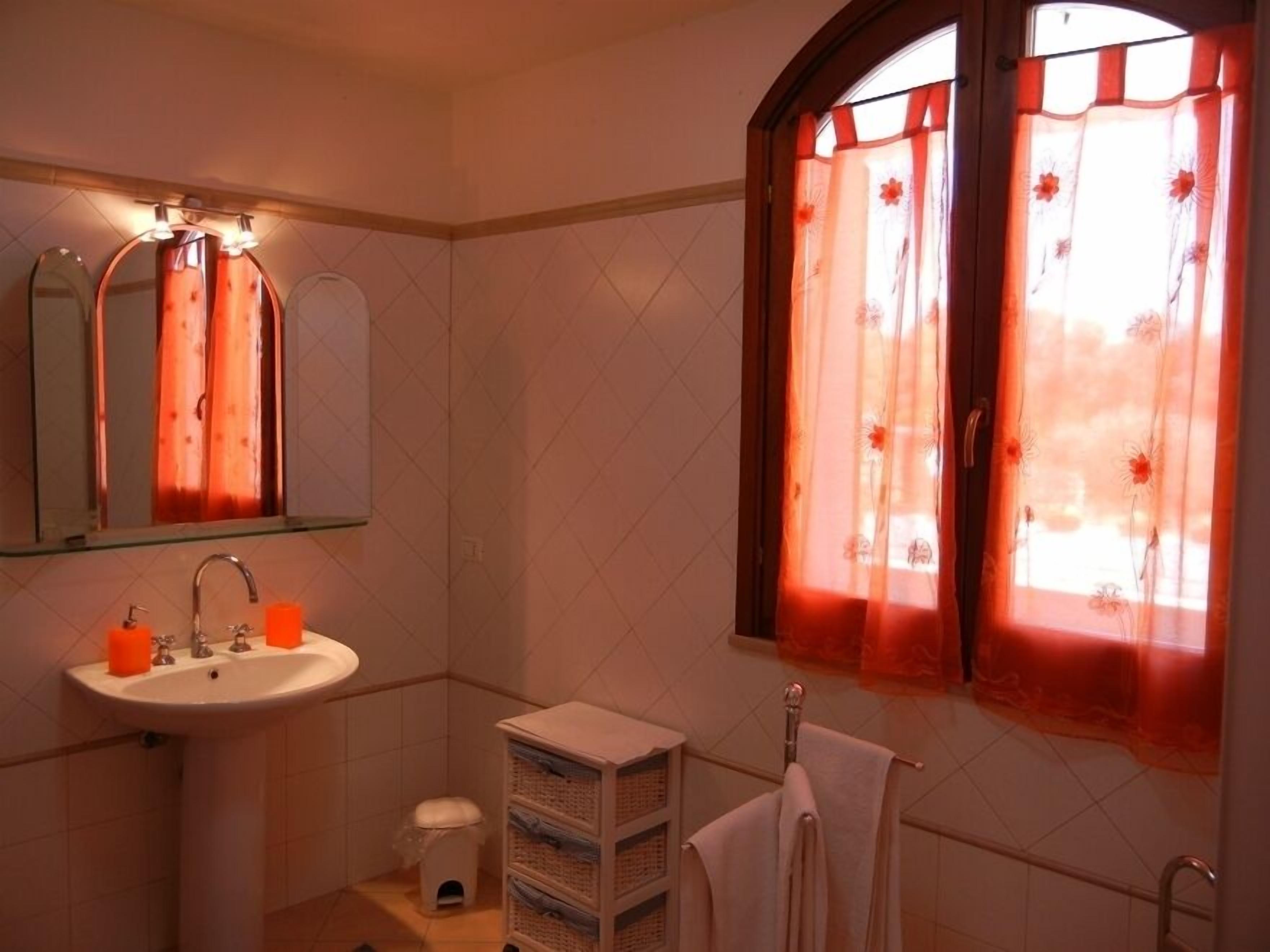A bathroom with a sink, mirror, and window with curtains.