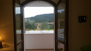 A balcony with a view of a green hillside and a yellow building. - Il Sogno di Alghero (Alghero)