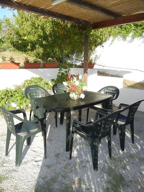 An outdoor patio with a round table and six chairs, surrounded by potted plants and a pergola. - Il Sogno di Alghero (Alghero)