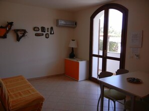 Una habitación con cama, mesa, silla, lámpara y ventana.