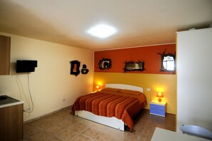 A bedroom with a bed, bedside lamps, a television on the wall, and a small desk area. - Il Sogno di Alghero (Alghero)