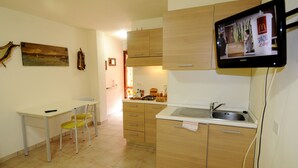 A compact kitchen with a dining area, a flat-screen TV mounted above the sink, and a wooden cabinet. - Il Sogno di Alghero (Alghero)