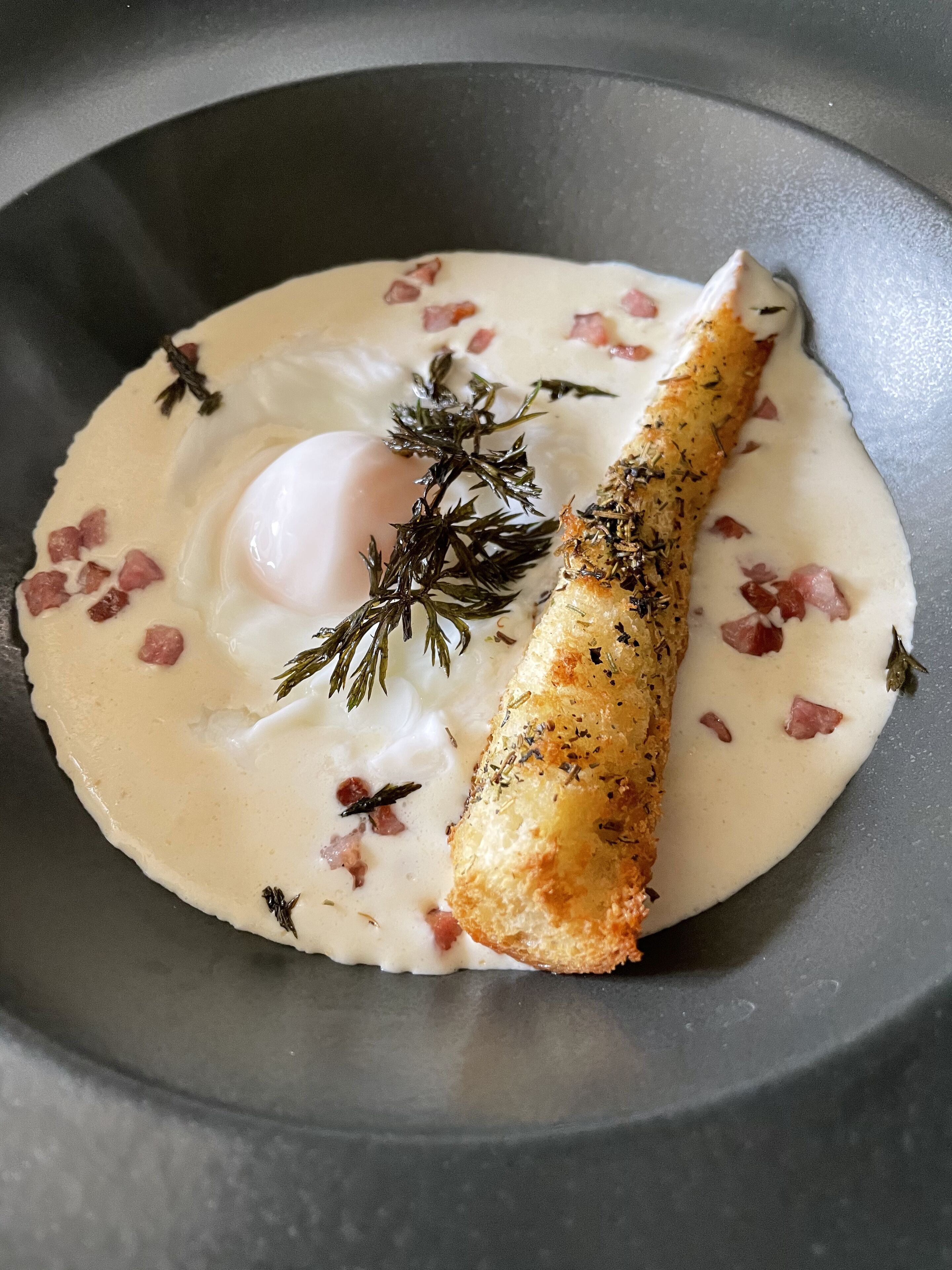 Un plat composé d’un œuf poché, de poisson et d’une sauce crémeuse, le tout garni d’herbes aromatiques.