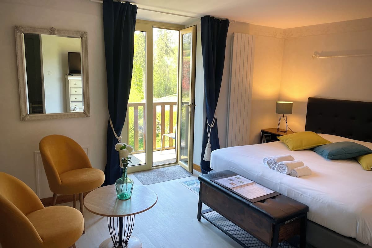 Quarto de hotel com cama, escrivaninha, cadeira, mesinha, espelho e vista para o exterior.