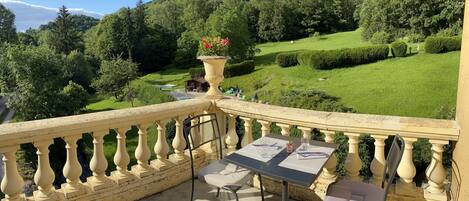 A balcony with a table and chairs, overlooking a lush green landscape with a mountain in the background.