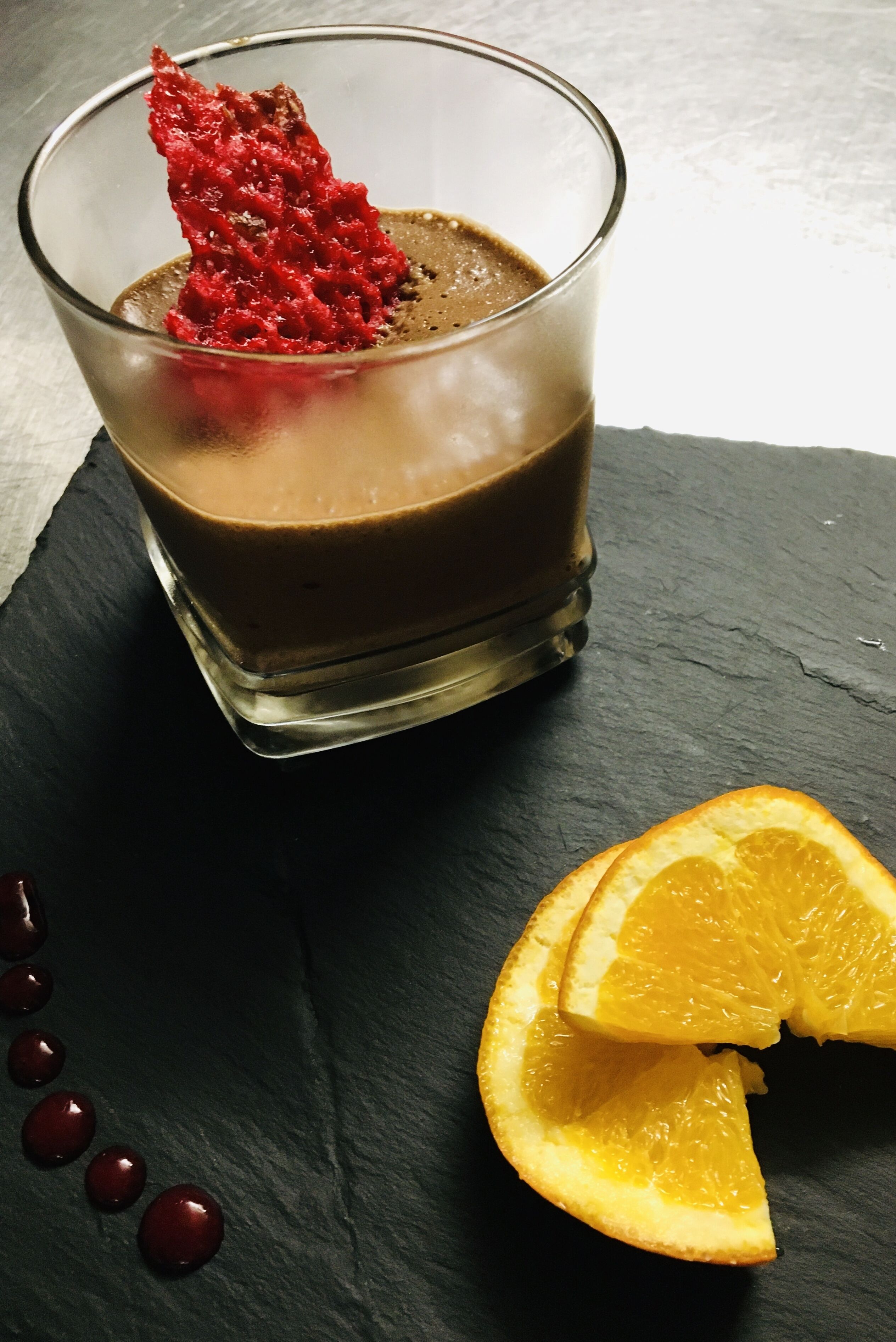 A glass of dark liquid with a red garnish on a black slate surface.