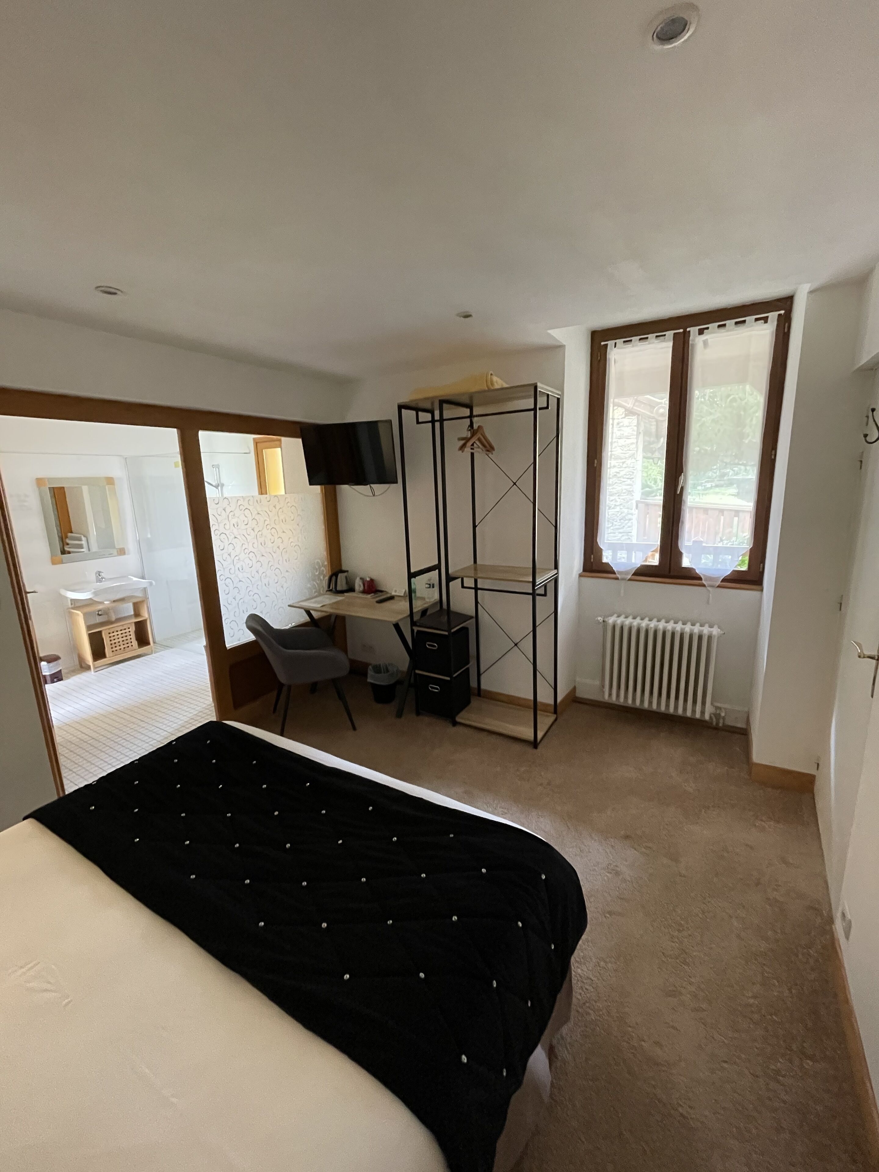 Un dormitorio con cama, escritorio, silla, televisor y ventana con cortinas.