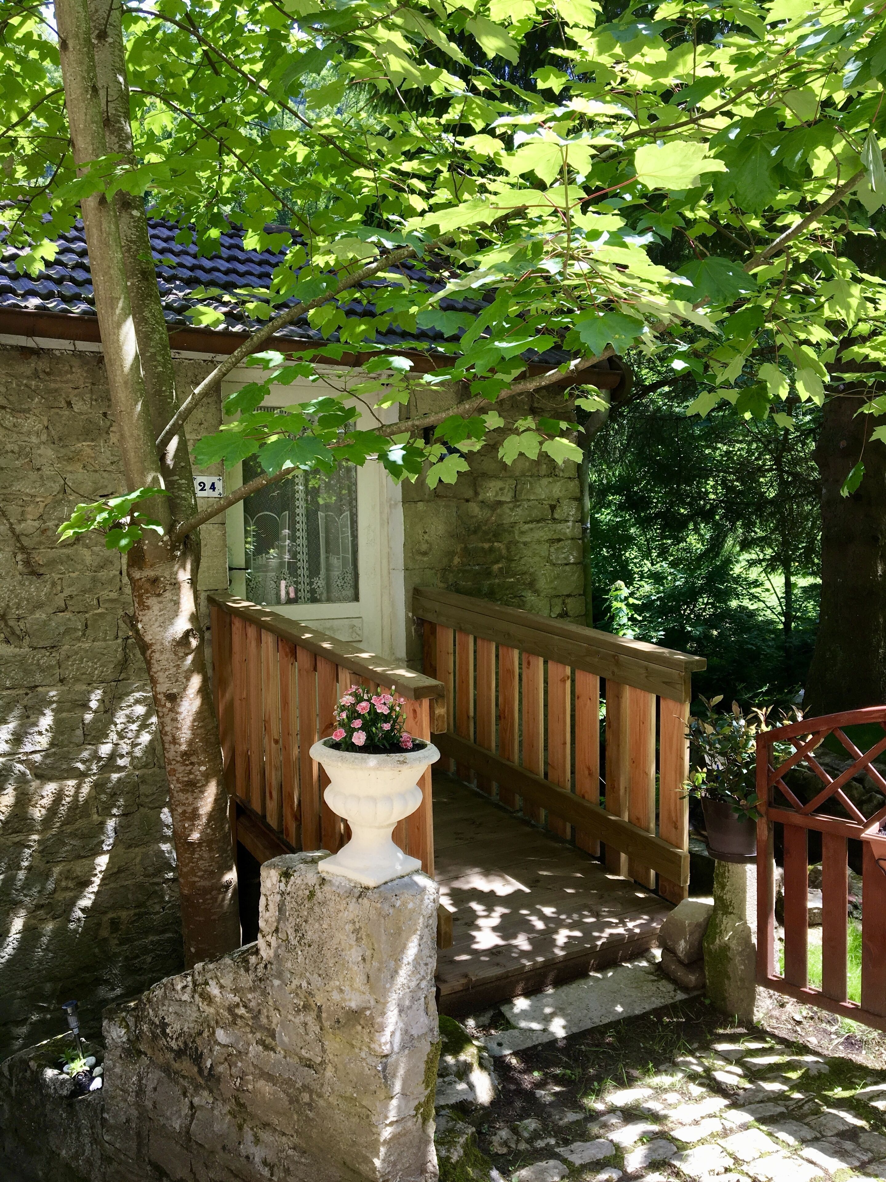 A stone staircase leading to a wooden deck with a railing, surrounded by greenery and a stone wall.