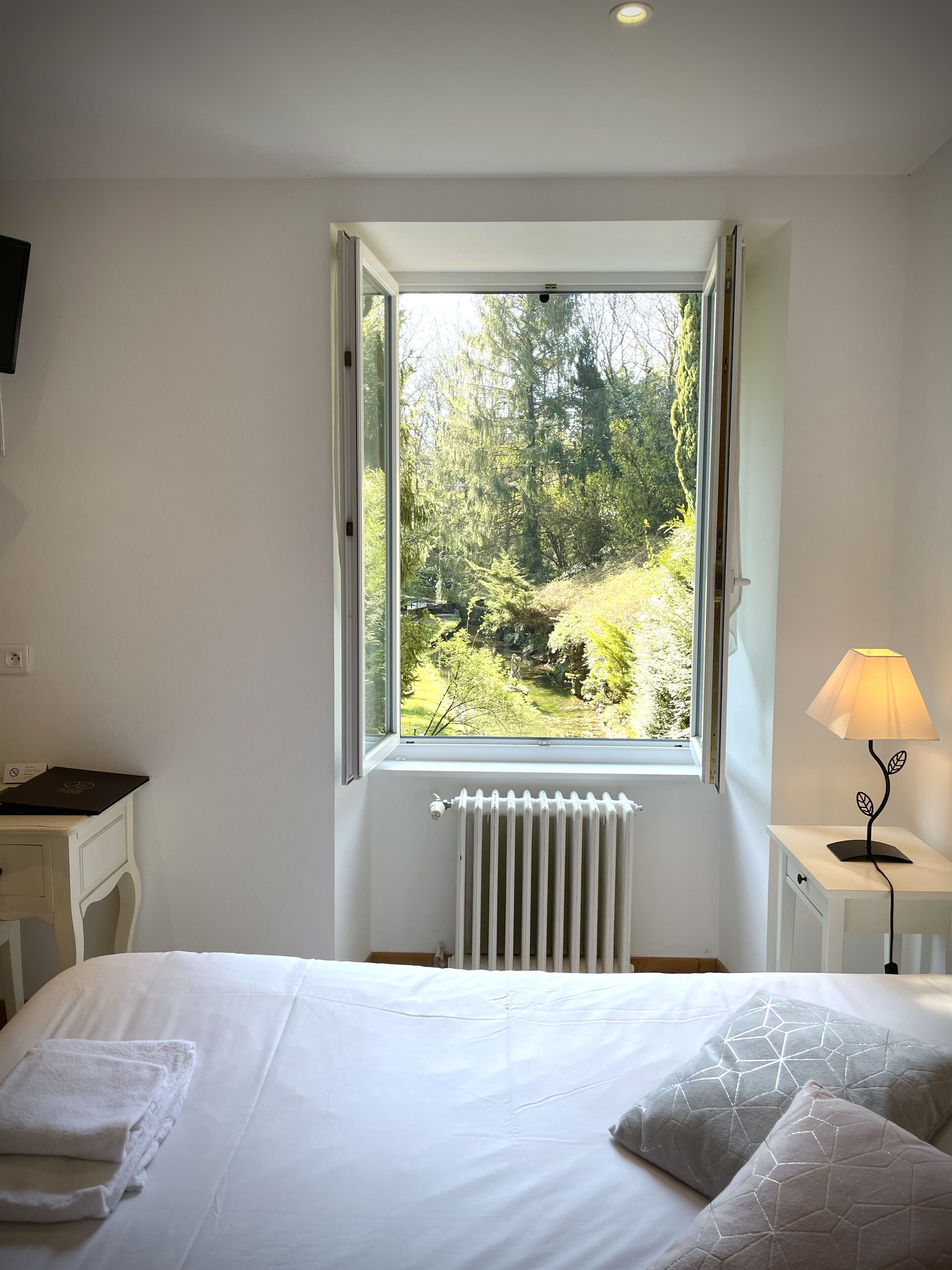 Une chambre avec une grande fenêtre, un radiateur, un bureau et une lampe.