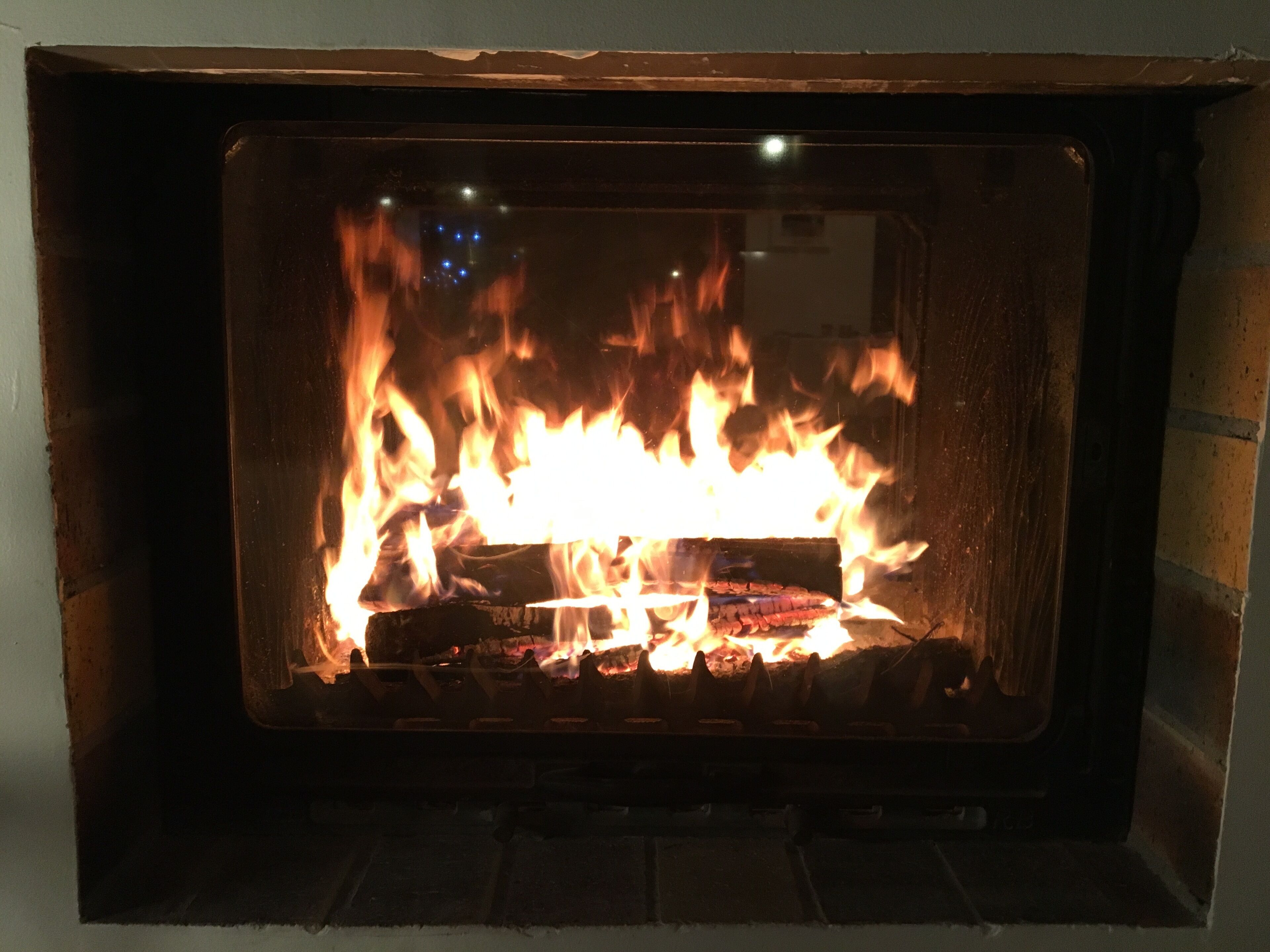 Une cheminée avec des flammes apparentes, un foyer en briques et un cadre en métal.