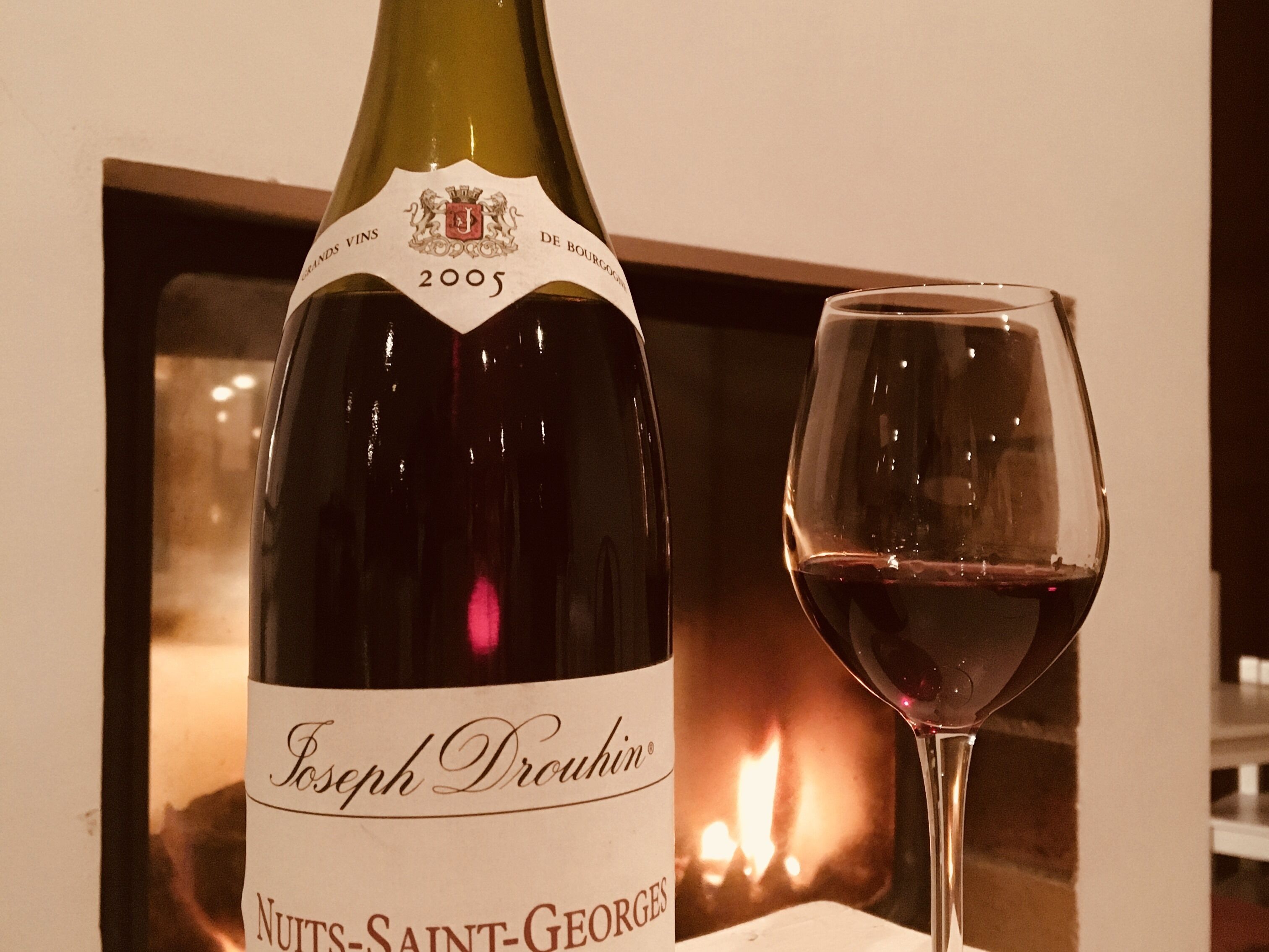A bottle of Joseph Drouhin Nuits-Saint-Georges wine from 2005 next to a glass of red wine.
