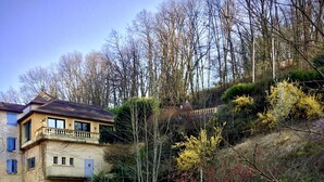 A house with a balcony overlooking a river, surrounded by trees and vegetation. - Hôtel de la Vallée Heureuse (Poligny)