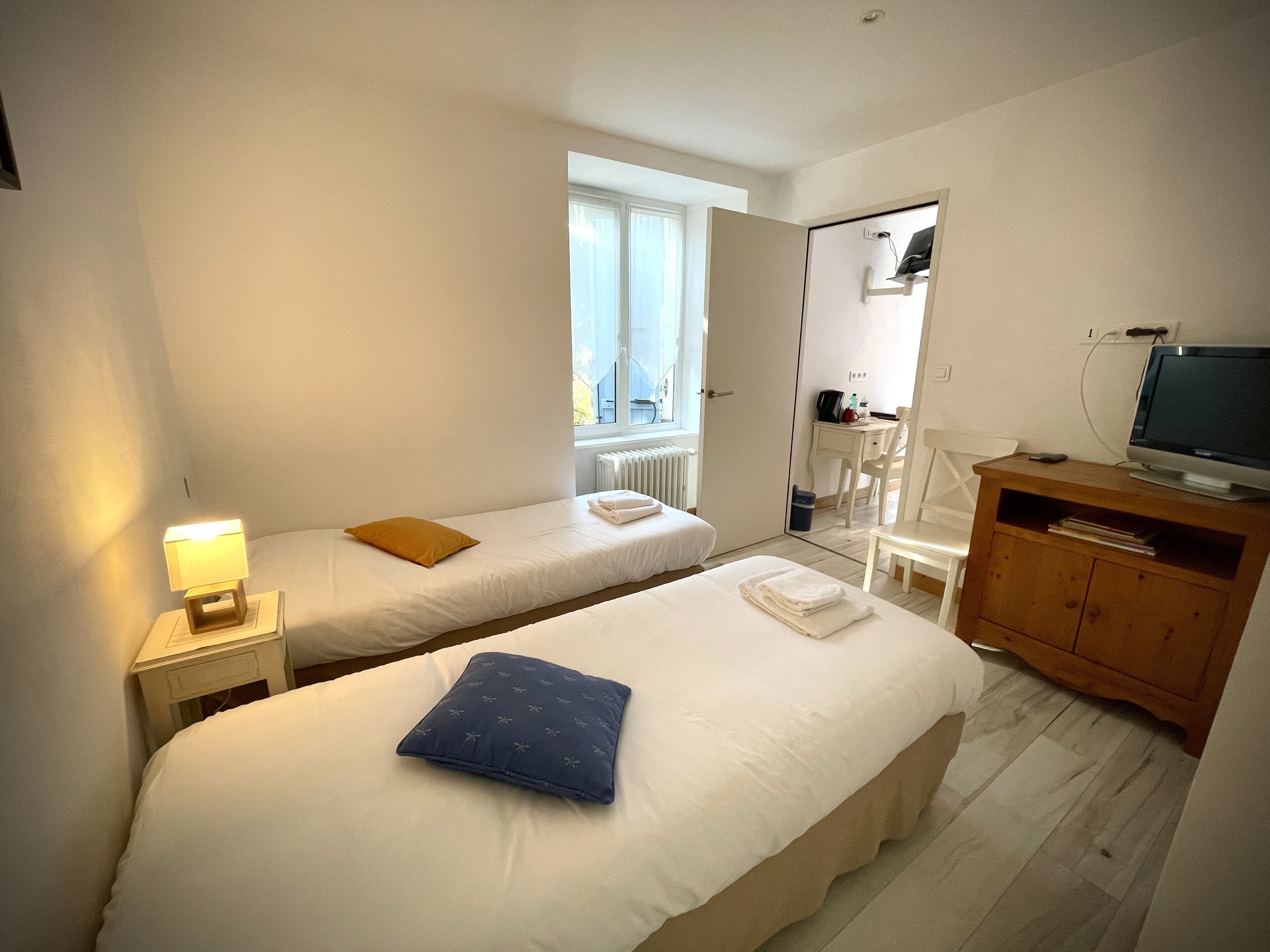 Una habitación de hotel con dos camas, un armario de madera con un televisor y una ventana que proporciona luz natural.