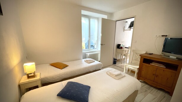 A hotel room with two beds, a wooden cabinet with a television, and a window providing natural light. - Hôtel de la Vallée Heureuse (Poligny)