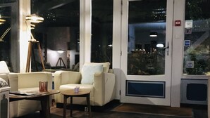 A cozy indoor seating area with a sofa, armchair, and coffee table, featuring a large window and a door with a glass panel. - Hôtel de la Vallée Heureuse (Poligny)