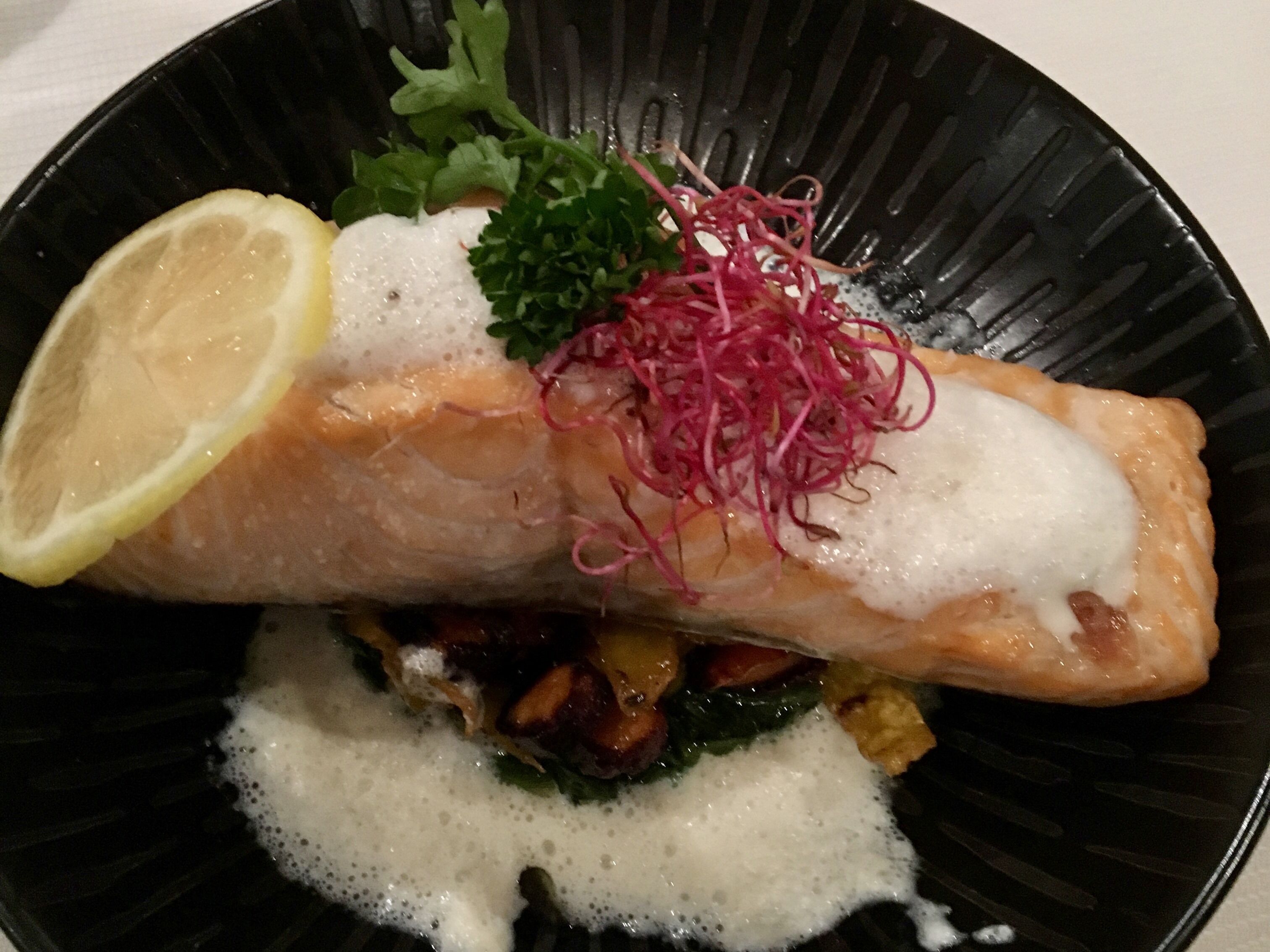 A plate with a salmon fillet, lemon, and greens.