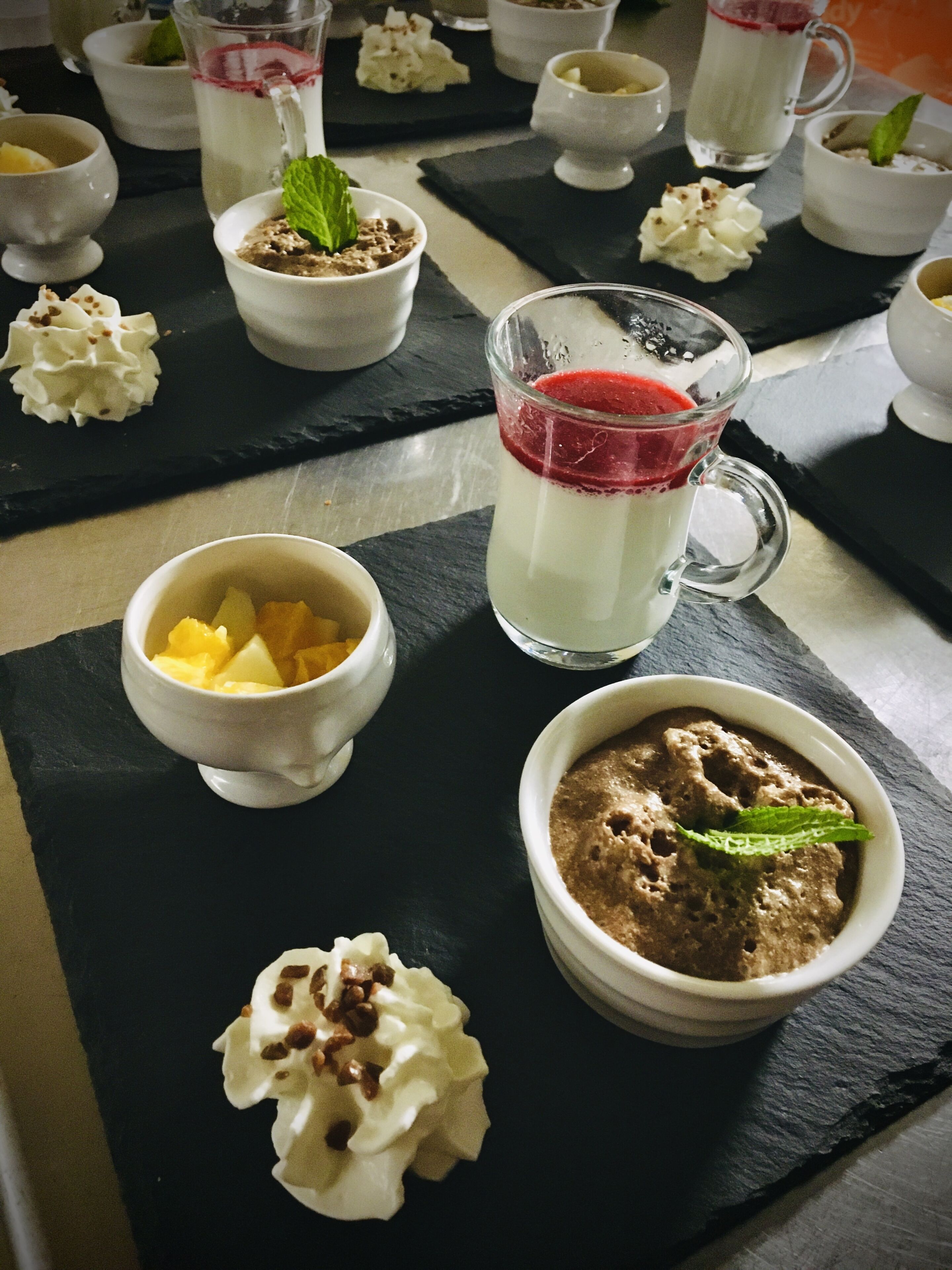 Una mesa de postres con diferentes opciones, incluyendo un vaso de bebida en capas, un bol de fruta y un postre de chocolate.