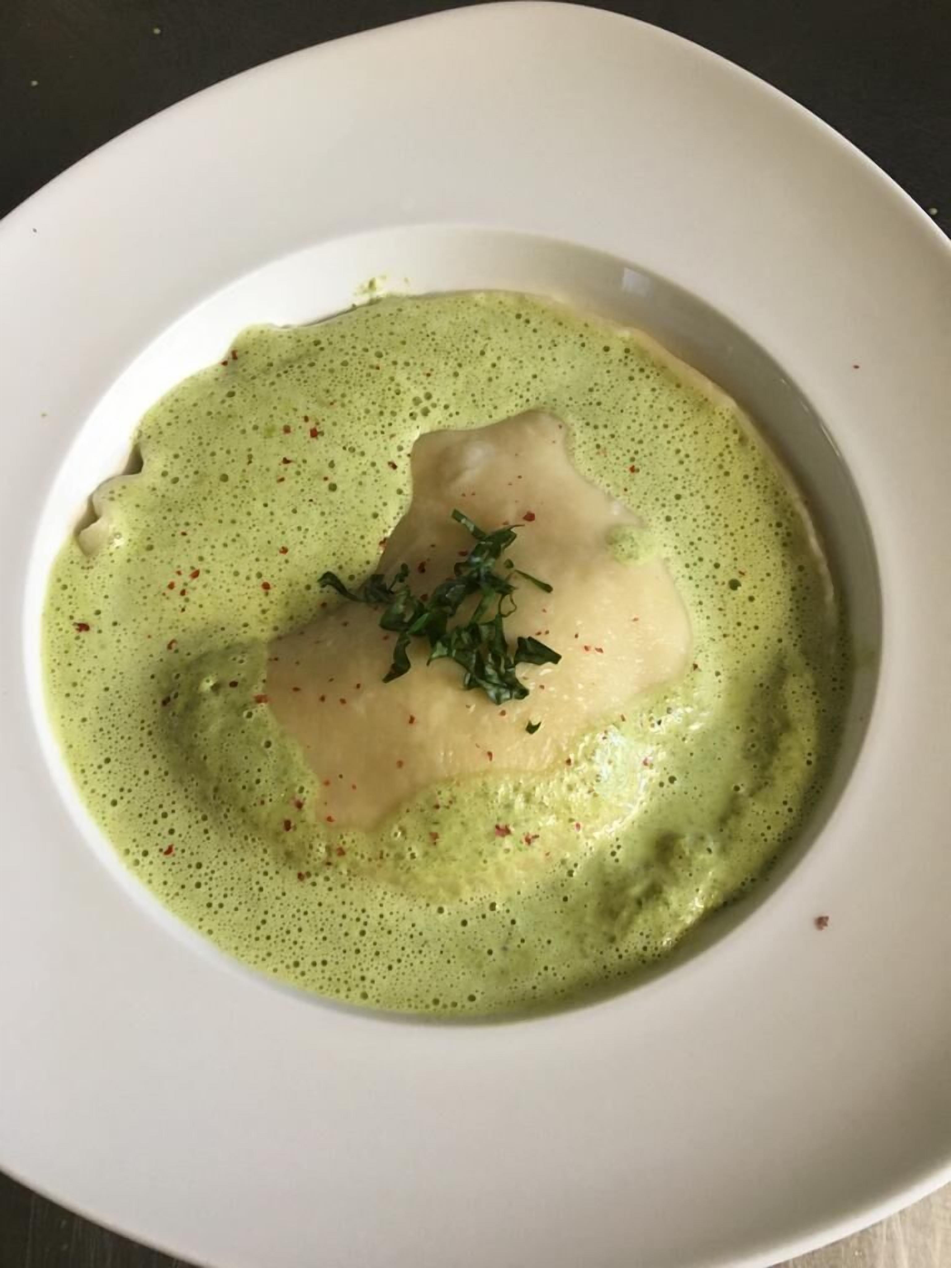 A white plate with a green sauce and a piece of food, possibly a dumpling, garnished with herbs.
