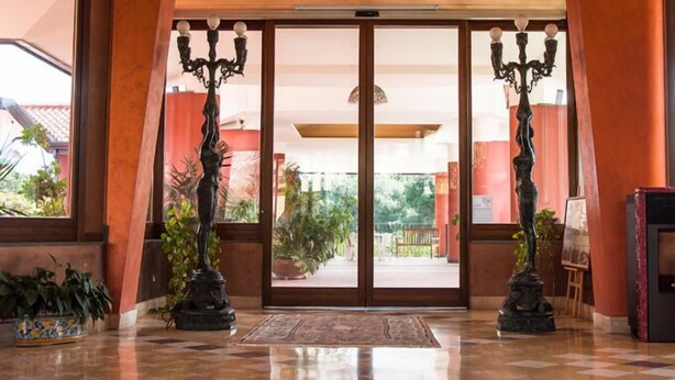 A hotel entrance with a glass door, potted plants, and a tiled floor. - Ares Hotel (San Giovanni la Punta)