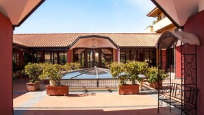 A covered courtyard with a glass-roofed central area, potted plants, and a seating area. - Ares Hotel (San Giovanni la Punta)
