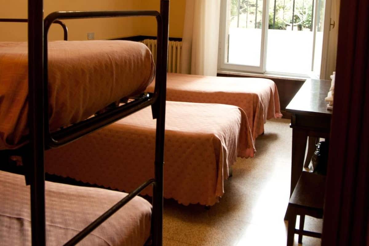 A dormitory room with bunk beds, a desk, and a window with curtains.