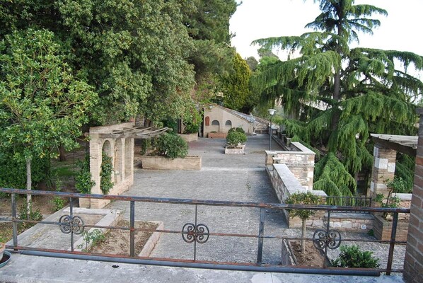 Un patio con construcciones de piedra, un pérgola y un pequeño edificio con ventanas arqueadas.
